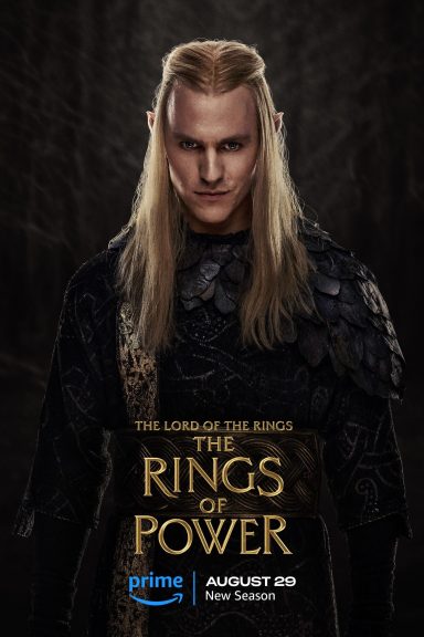 A character with long blond hair, wearing dark, ornate attire, set against a shadowy background.